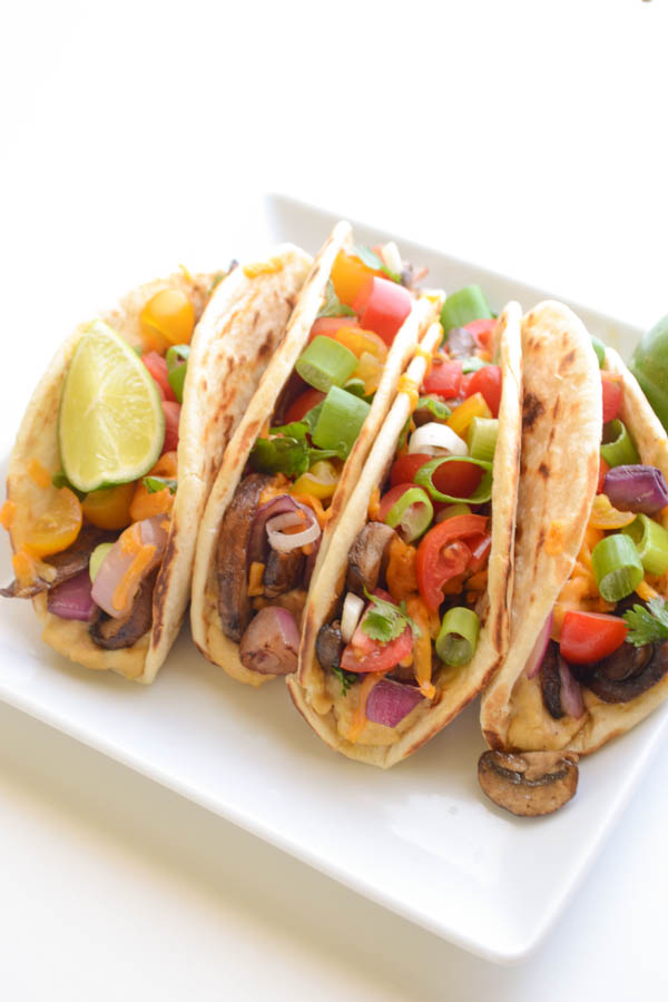 Loaded with roasted veggies like thick rings of sweet onion and mushrooms layered on top of garlicky hummus and melty cheddar, these Hummus Tacos are vegetarian taco perfection | onesimplefeast.com